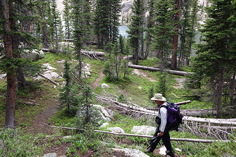 Hiker descending along a thin trail to lake below