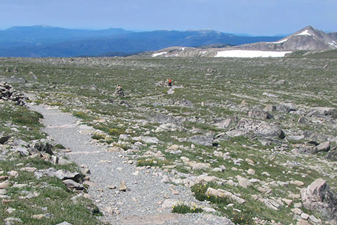 Hiker seen in the distance at the end of a trail. Hiker is wearing an orange jacket